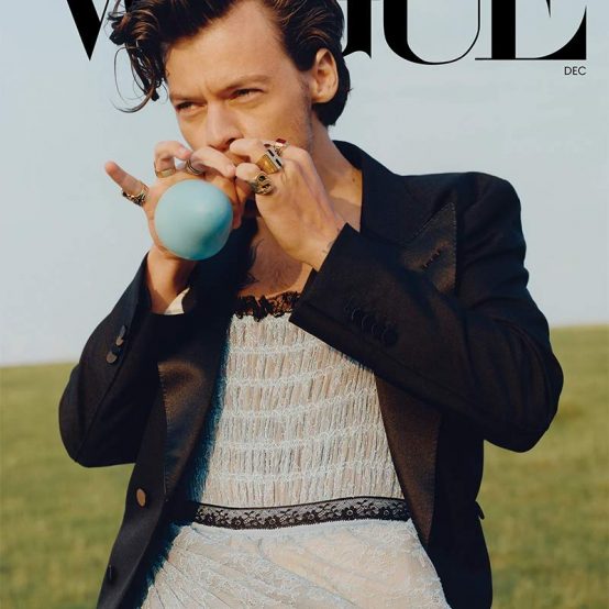 Harry Styles for Vogue wearing a dress and tuxedo blowing up a balloon